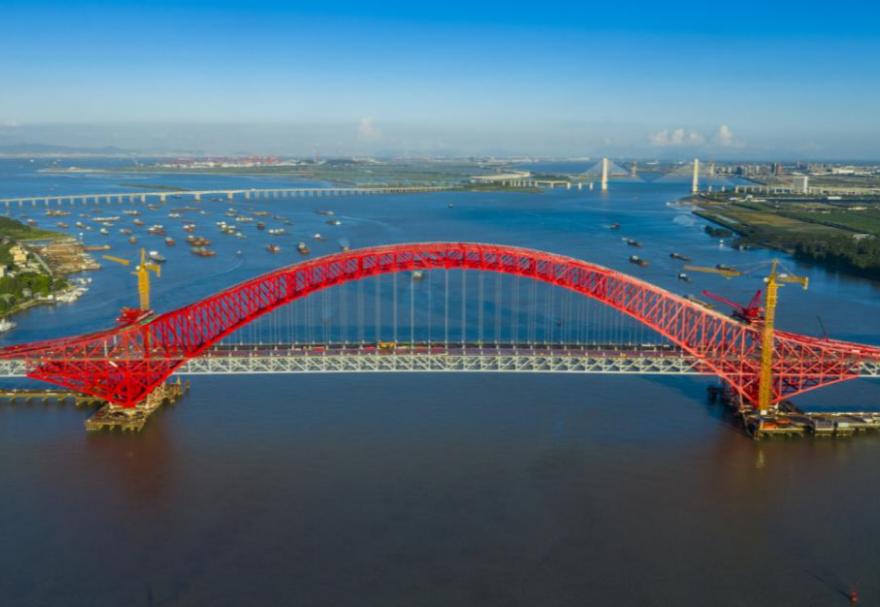 明珠灣大橋位于廣州市南沙區(qū)龍穴南水道之上，是粵港澳大灣區(qū)的重要連接通道。大橋工程全長約10.42公里，主線全長約9.1公里，主橋采用中承式六跨連續(xù)鋼桁拱橋，全長1016米，為同類型橋梁最大跨度。氣勢恢宏的明珠灣大橋綿延伸向遠方，將南沙多條核心主干道緊緊連在一起，構筑了明珠灣區(qū)內(nèi)部核心交通環(huán)，是廣州面向粵港澳大灣區(qū)建設的交通樞紐工程和地標性建筑。圖為南沙明珠灣大橋。